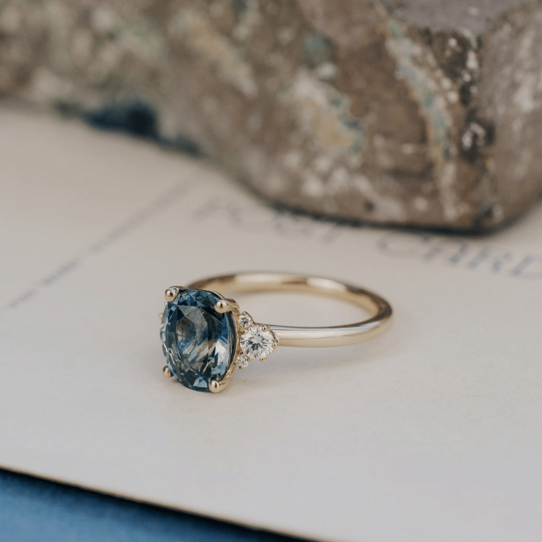 A 14k gold ring featuring a blue sapphire gemstone viewed from the side, displayed on a textured white surface.