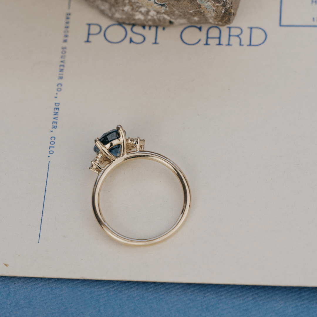 A 14k gold ring featuring a blue sapphire gemstone viewed from the top, displayed on a textured white surface.