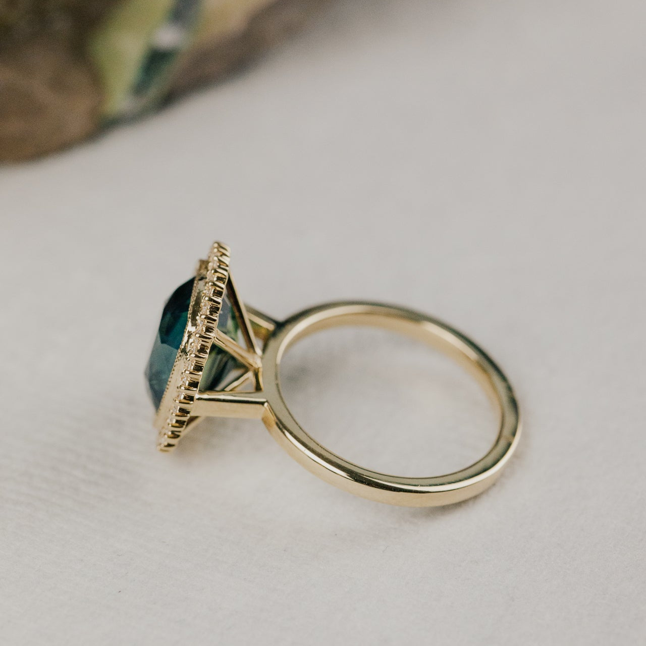 Side profile of a gold ring with a elongated cushion cut green Madagascar sapphire center stone  on a light background