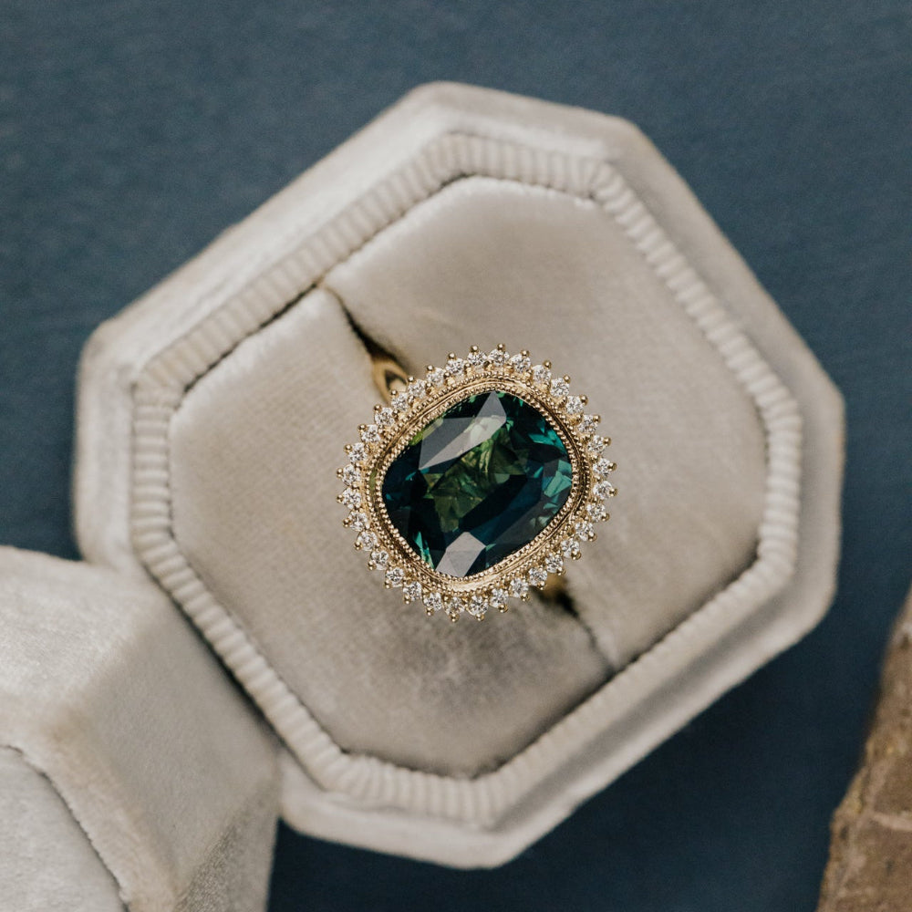 Gold diamond halo ring with a elongated cushion cut green Madagascar sapphire center stone  in a hexagonal box on a dark background