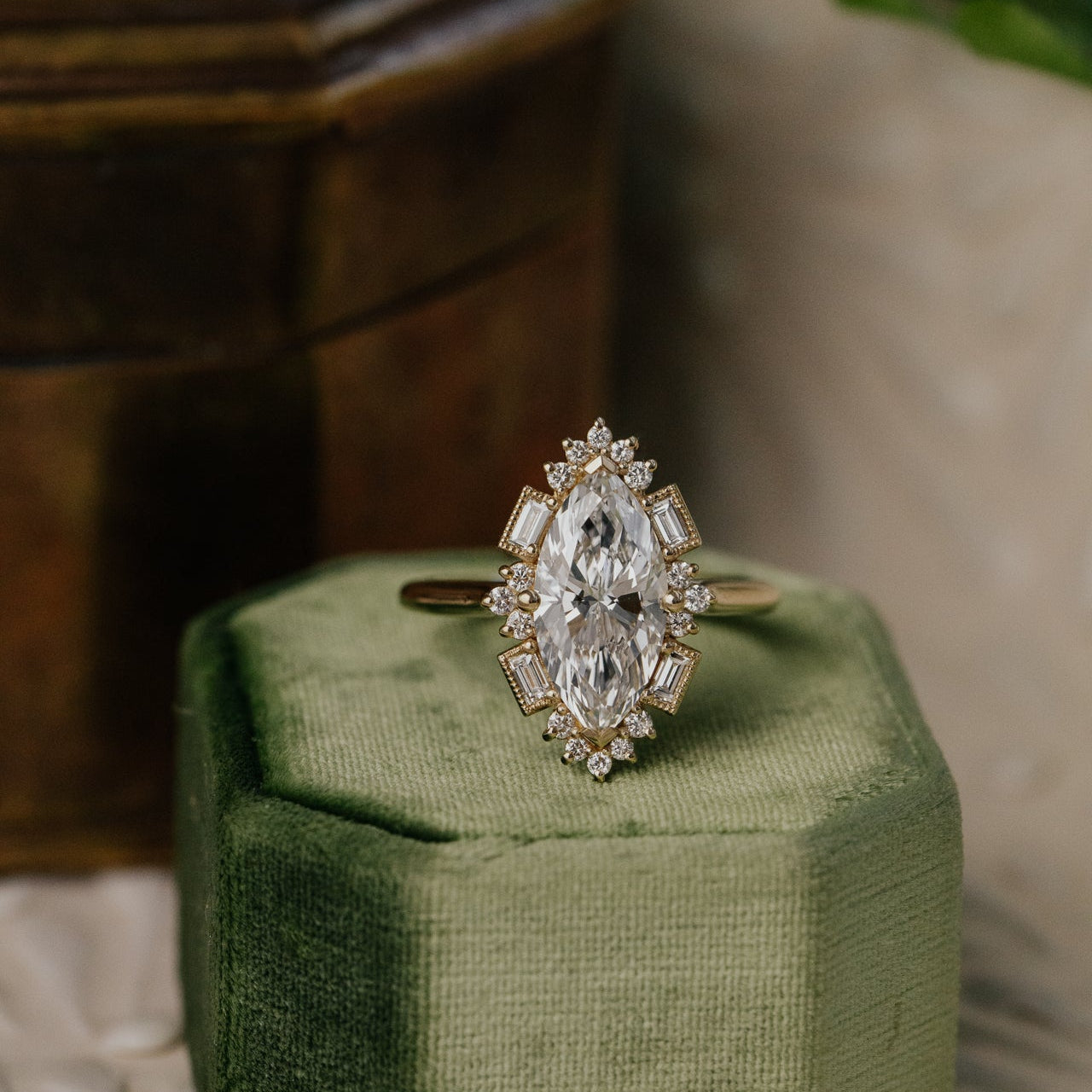 Agave marquise diamond halo ring on a green cushion with a blurred background.