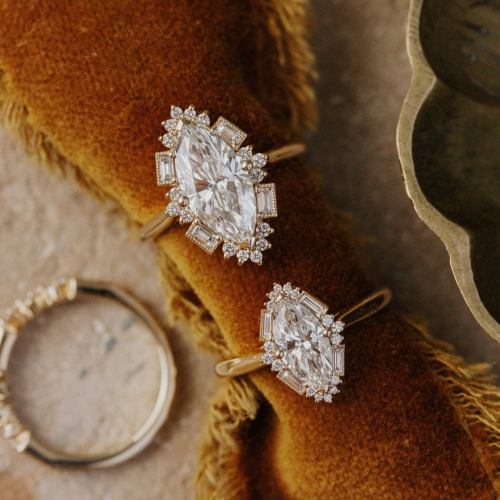 Pair of diamond Agave marquise rings on a brown textured surface.