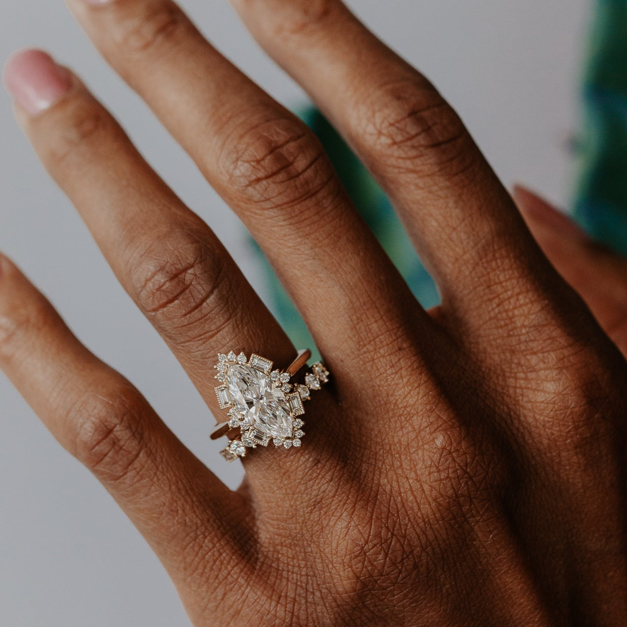 Hand wearing a marquise diamond Agave engagment ring with a blurred background.
