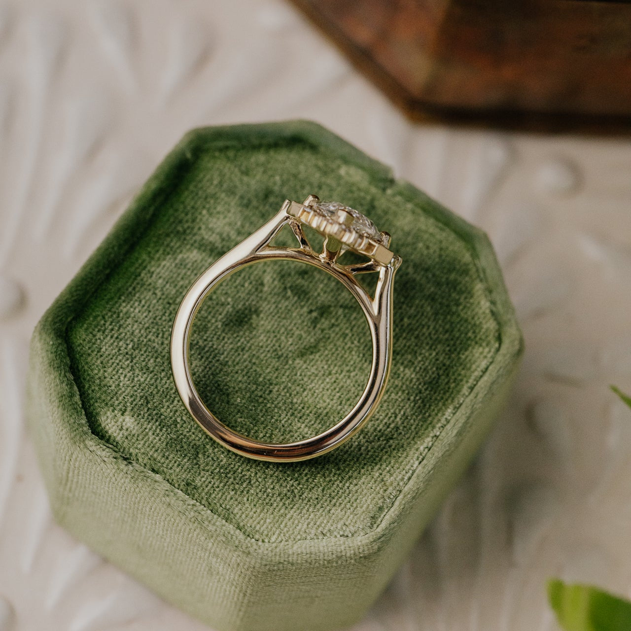 Gold Agave engagement ring with a marquise diamond on a green velvet cushion.