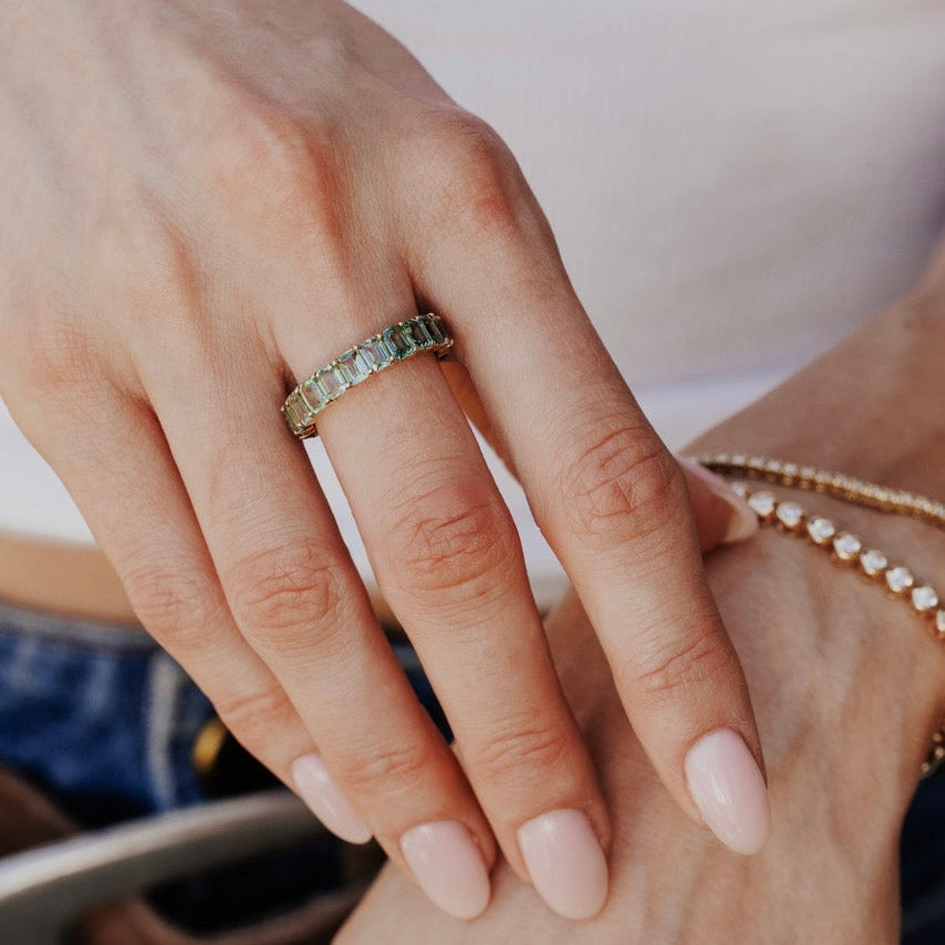 Close-up of a hand with a amara green sapphire band on a blurred background.