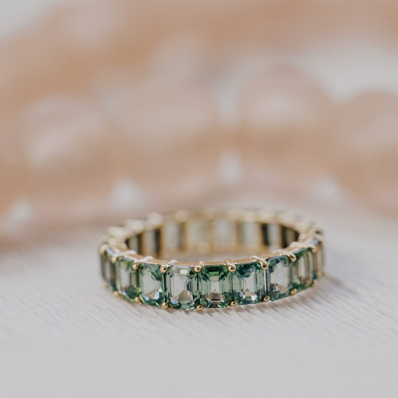 Gold band with green sapphires on a textured surface.
