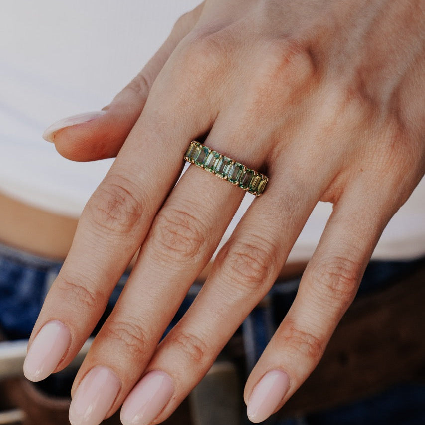 Close-up of a hand wearing a green sapphire band with a blurred background.