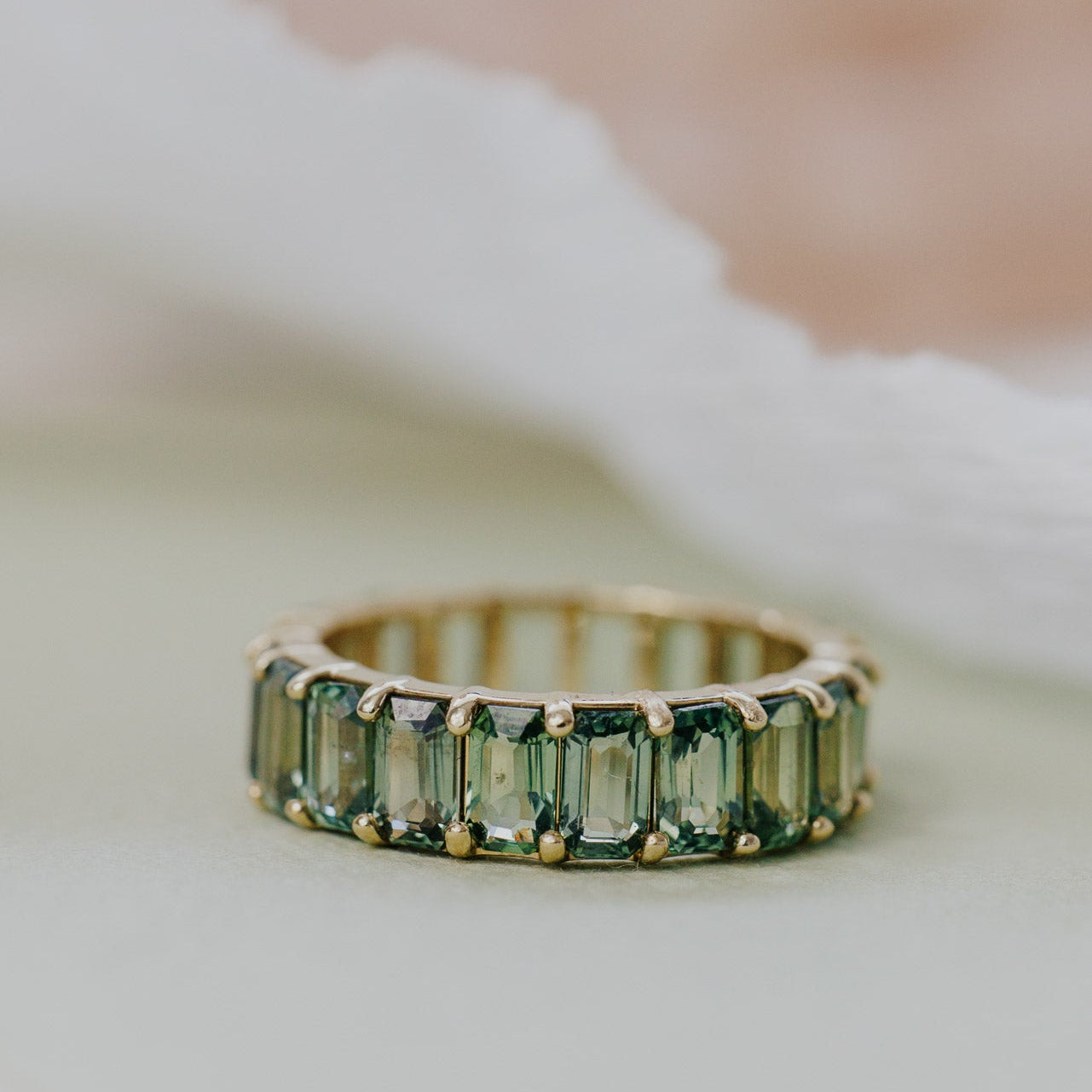 Gold band with green sapphires on a soft white background.