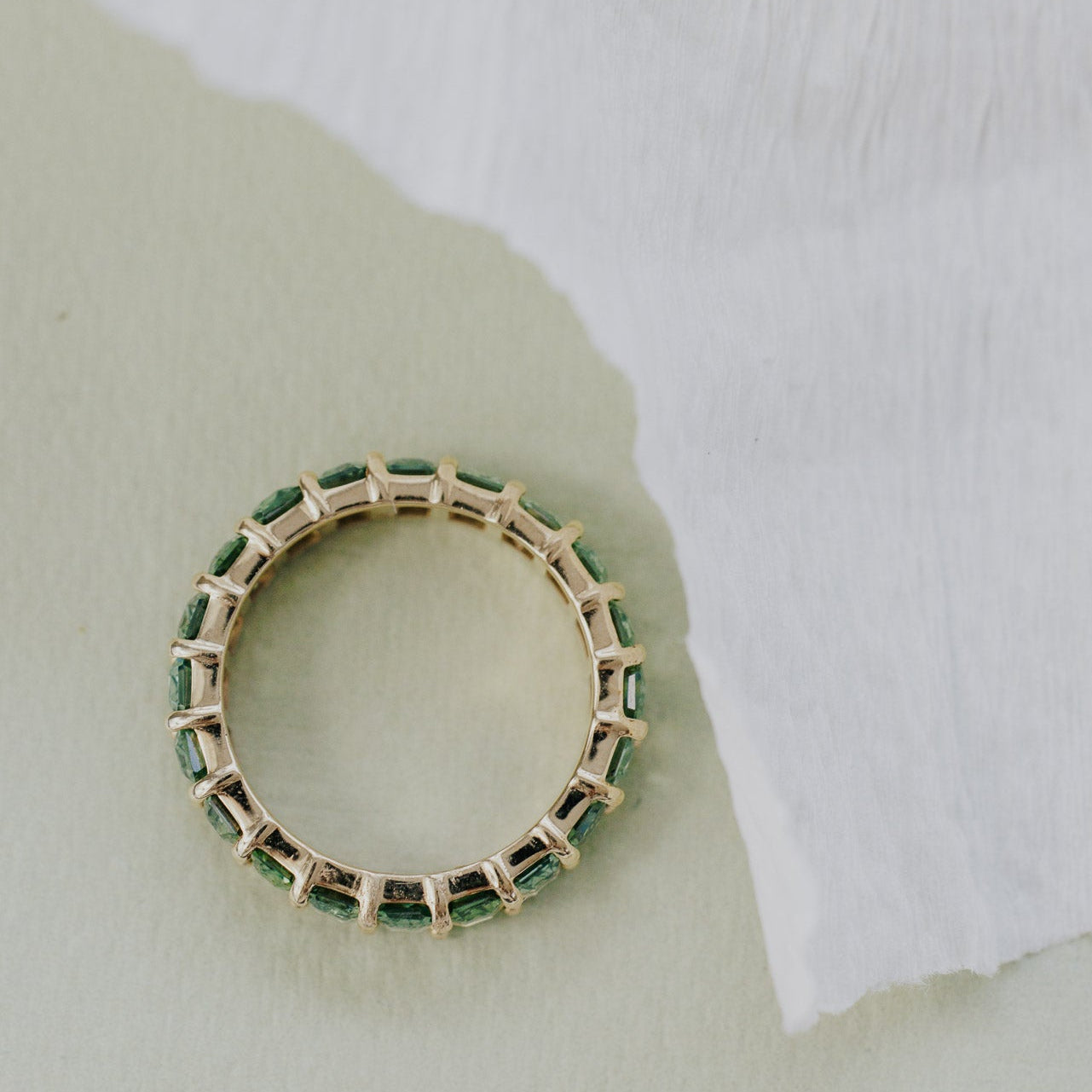 Gold band with green sapphires on a textured white and green background.