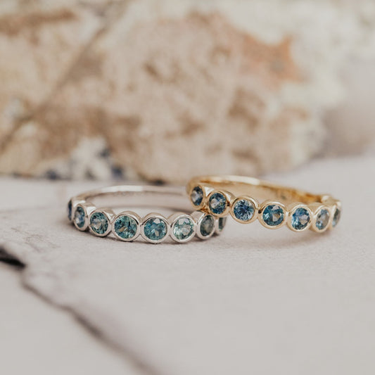 Two Aster bands in white and yellow gold with round Montana sapphires on a white background.
