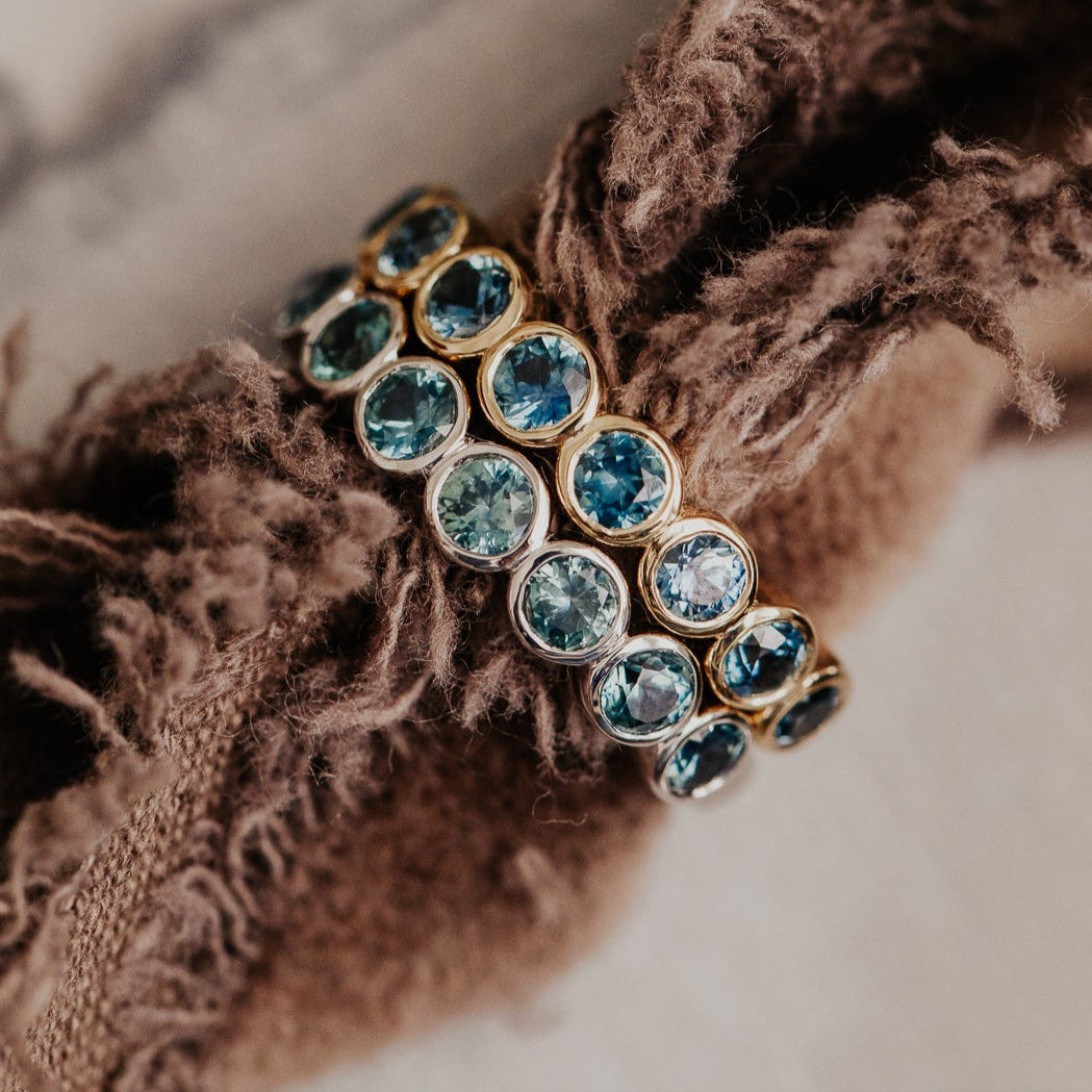 Gold Aster band with blue Montana sapphire gemstones on a textured fabric background.