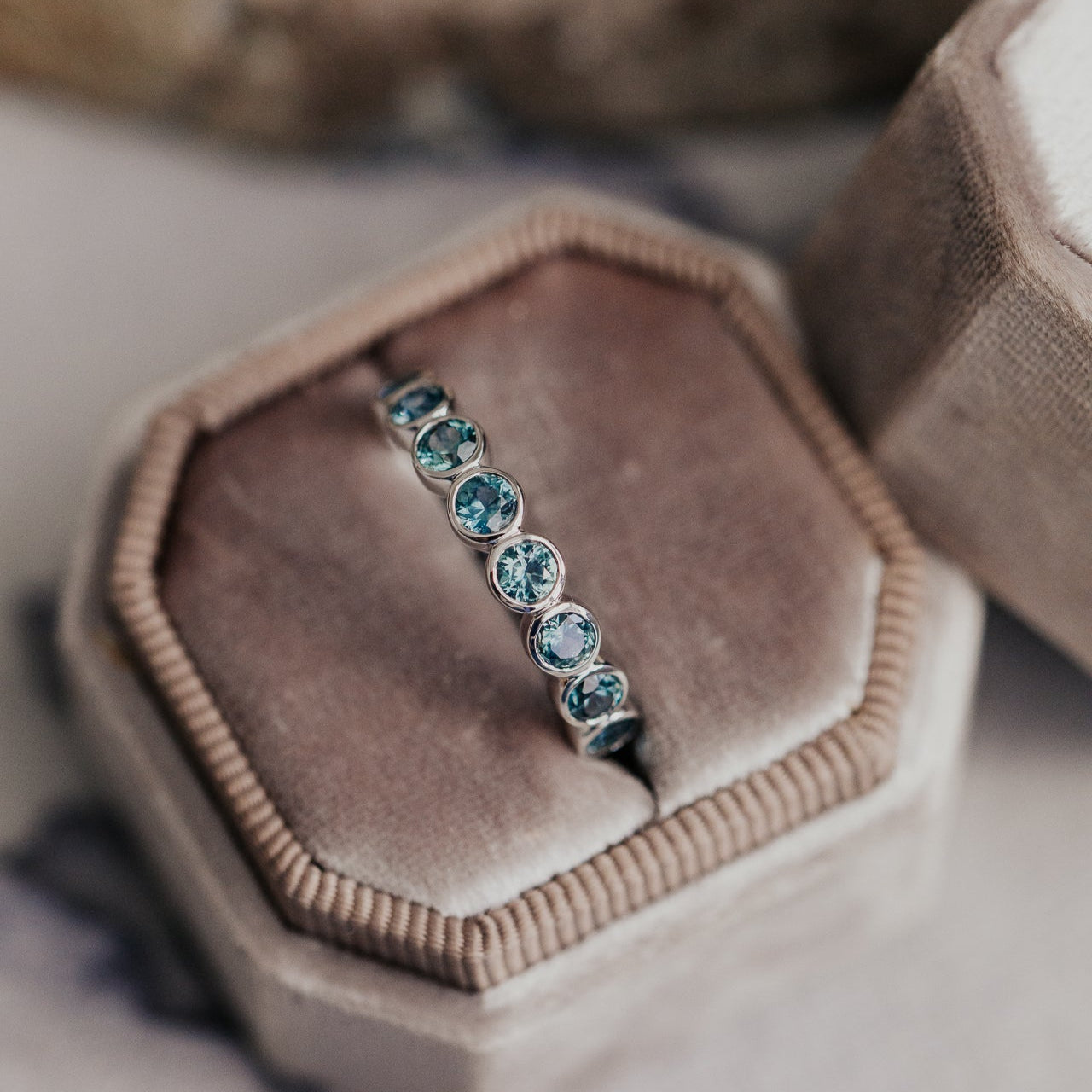 Close up of a white gold Aster Montana sapphire band in a grey velvet ring box.