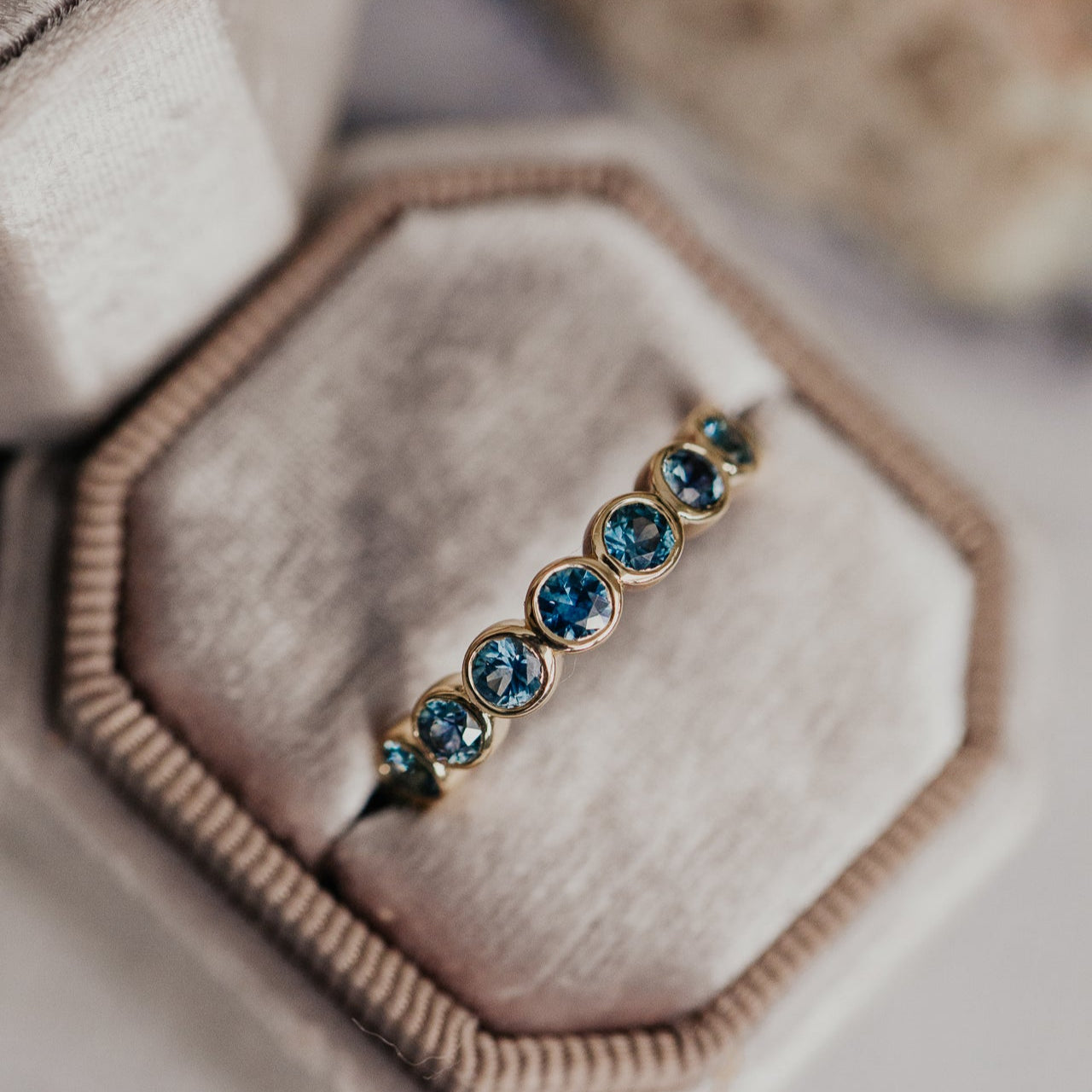 Close up of a gold Aster Montana sapphire band in a grey velvet ring box.