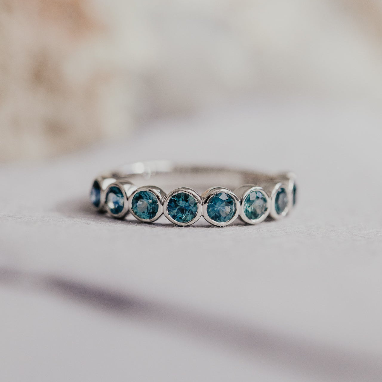 Close up of a white gold Aster Montana sapphire band on a white background.