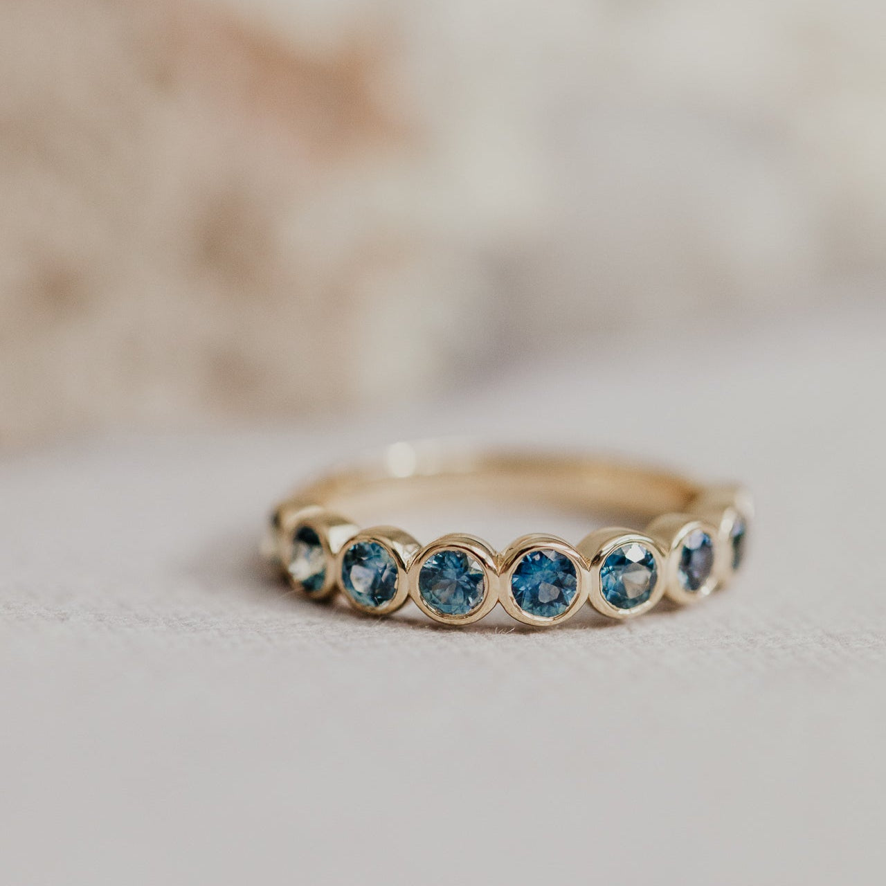 Close up of a gold Aster Montana sapphire band on a white background.