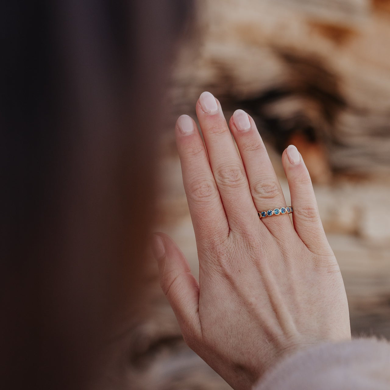 Close up of a person wearing a gold Aster Montana sapphire band with a blurred background.