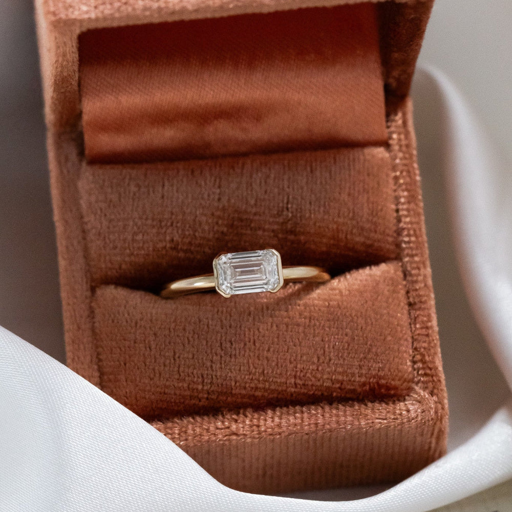 Austen diamond ring in an open brown velvet box on a white surface with a piece of paper.