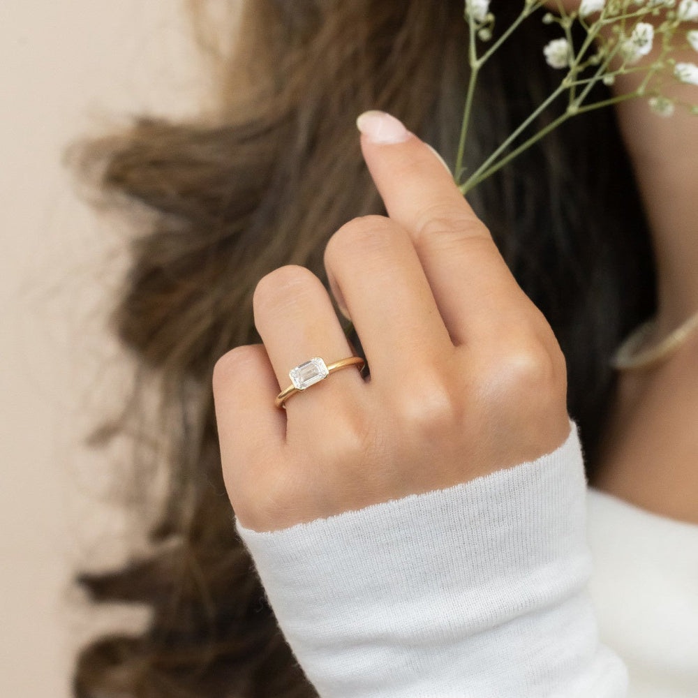 Hand wearing a gold Austen ring with a diamond, holding a small bouquet of flowers.