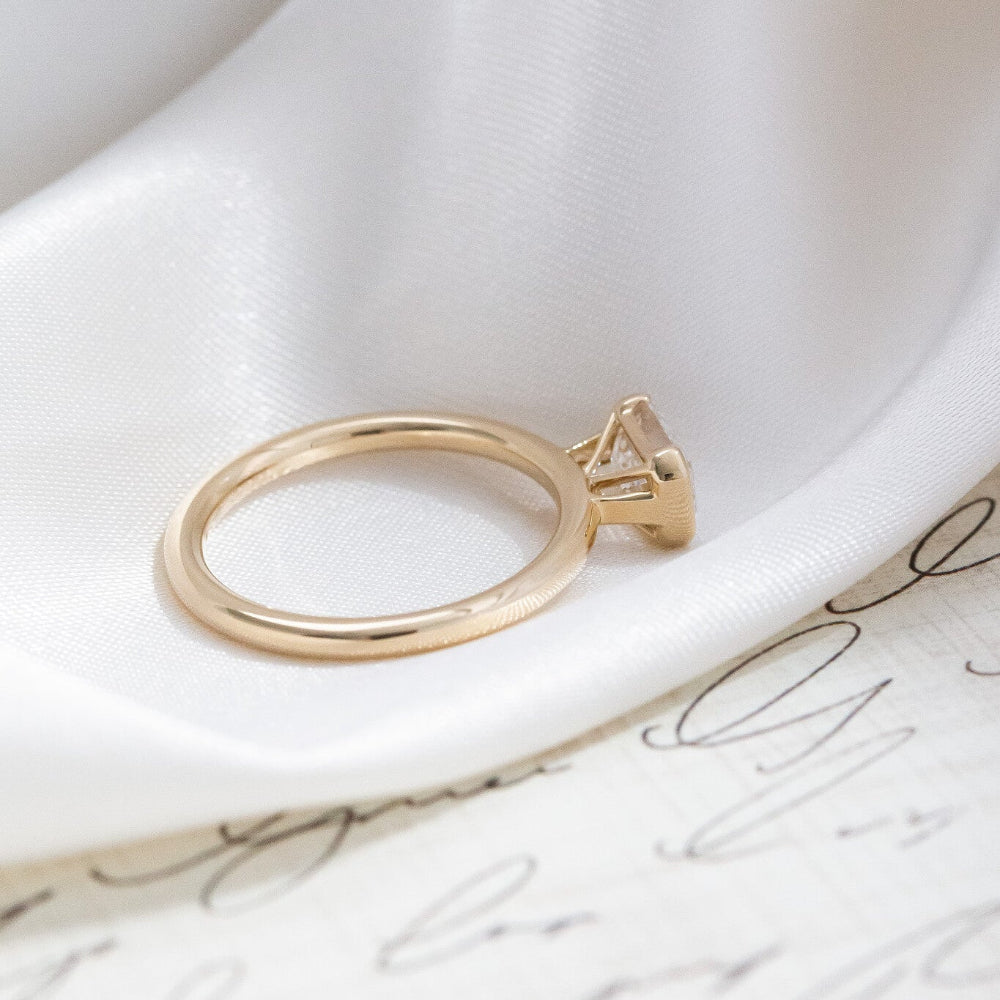Gold Austen ring with a emerald-cut diamond on a white surface.