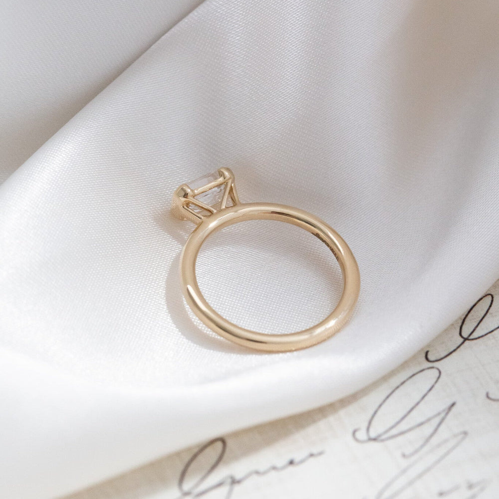Gold Austen engagement ring on a white fabric surface.