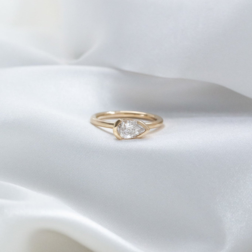 Gold Austen ring with a pear diamond on a white satin background.