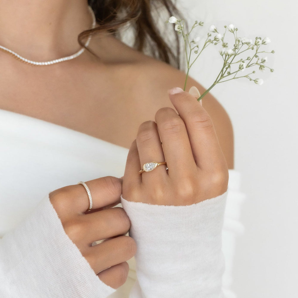 Close-up of a woman's hand wearing a Austen pear ring and a diamond band with a white background.