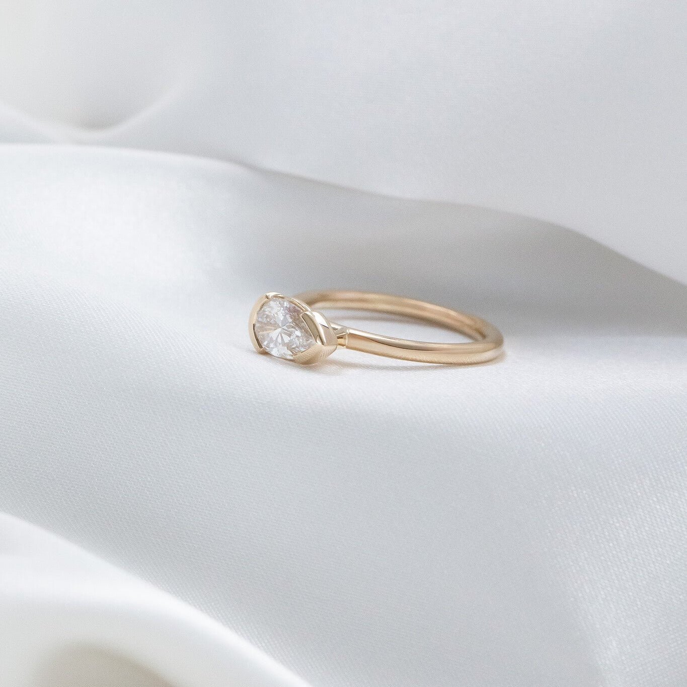 Gold Austen ring with a diamond on a white, wavy surface.