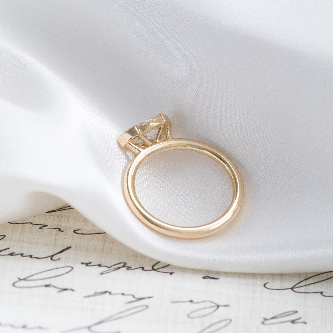 Gold Austen pear diamond engagement ring on a white fabric surface with cursive text.