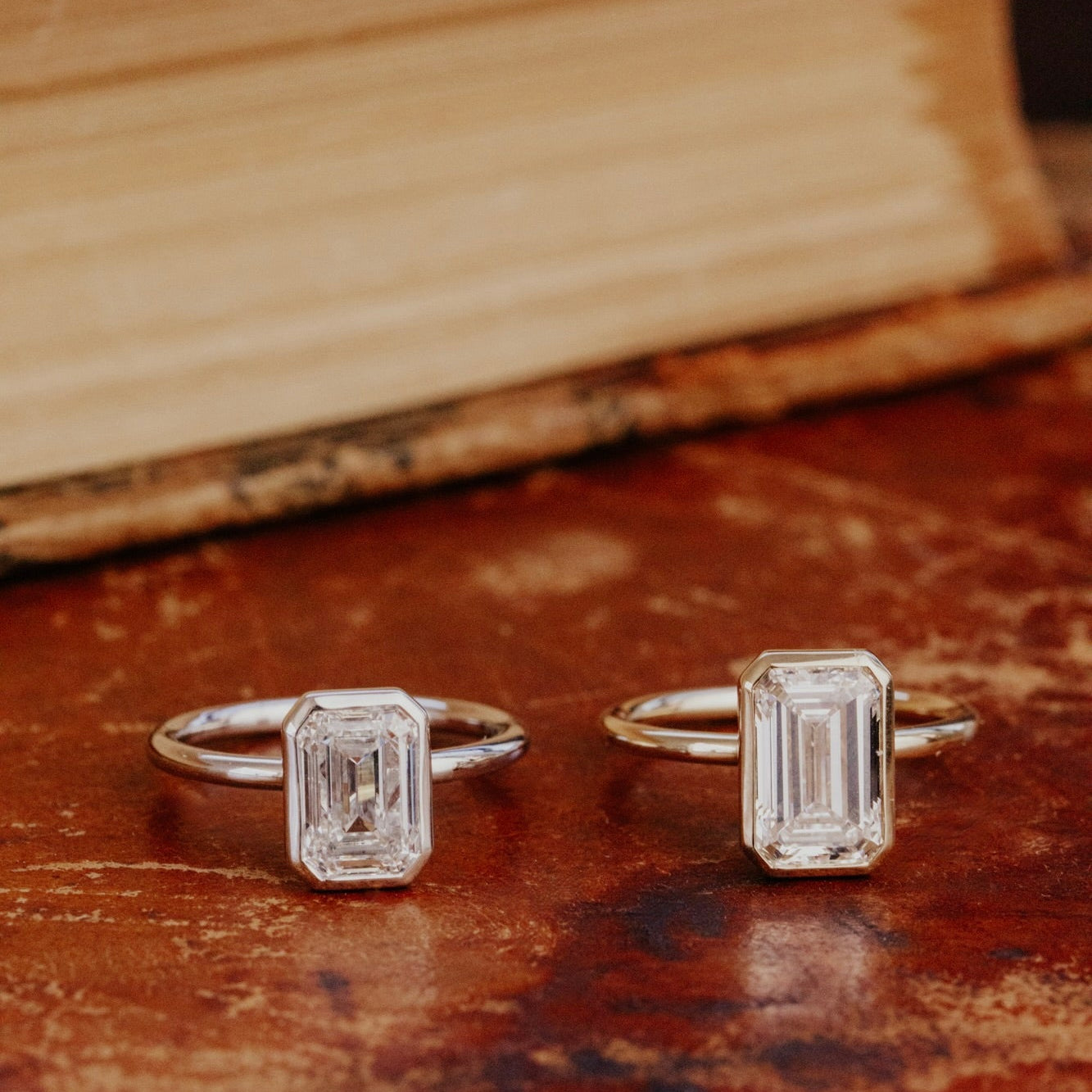 Two Bailey emerald cut diamond rings in different carat weights on an old book.