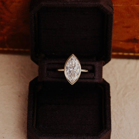 Bailey marquise diamond ring in a black velvet box on a wooden surface.