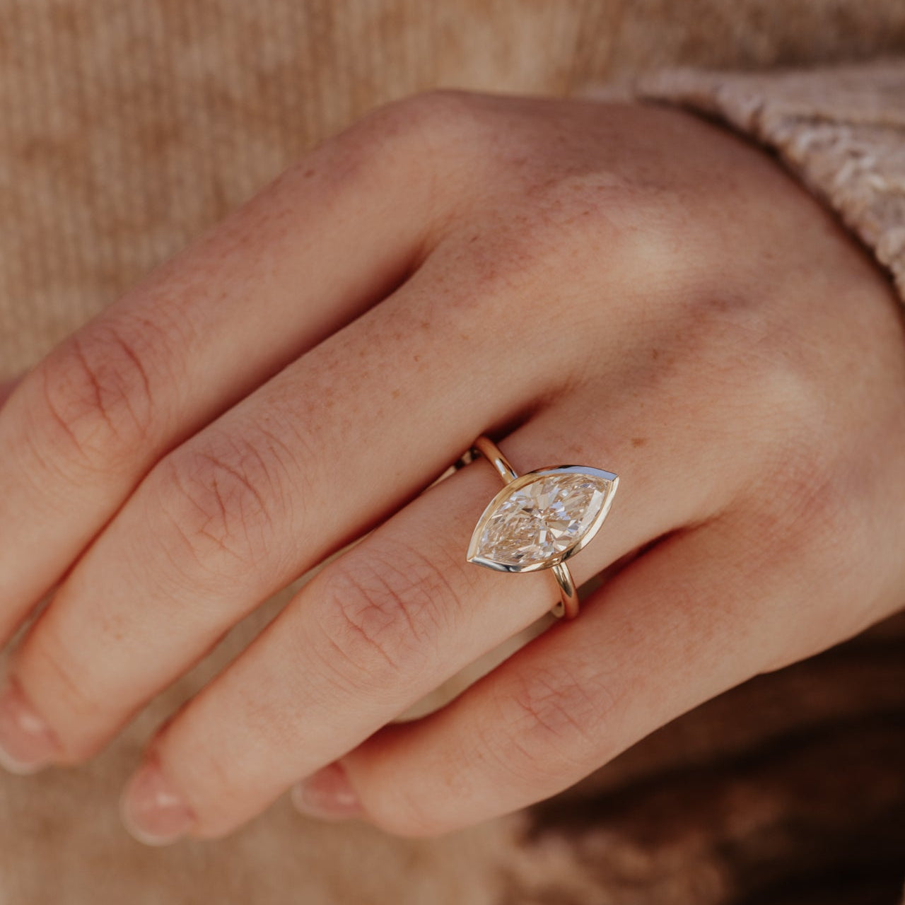 Close-up of a hand wearing a yellow gold Bailey ring with a marquise-shaped diamond.