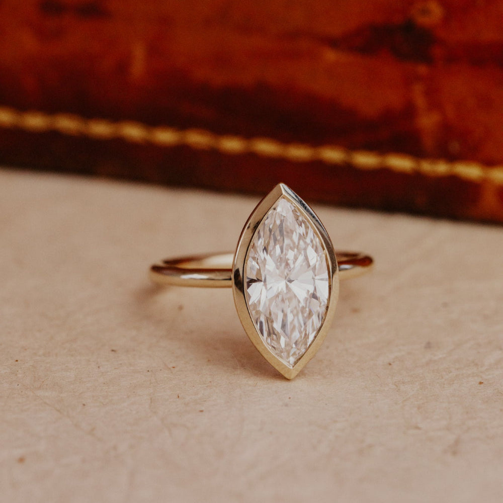 Gold Bailey ring with a large marquise diamond on a textured surface.