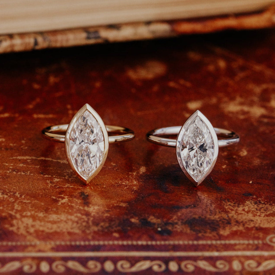 Two Bailey marquise diamond rings in yellow and white gold on an antique book.