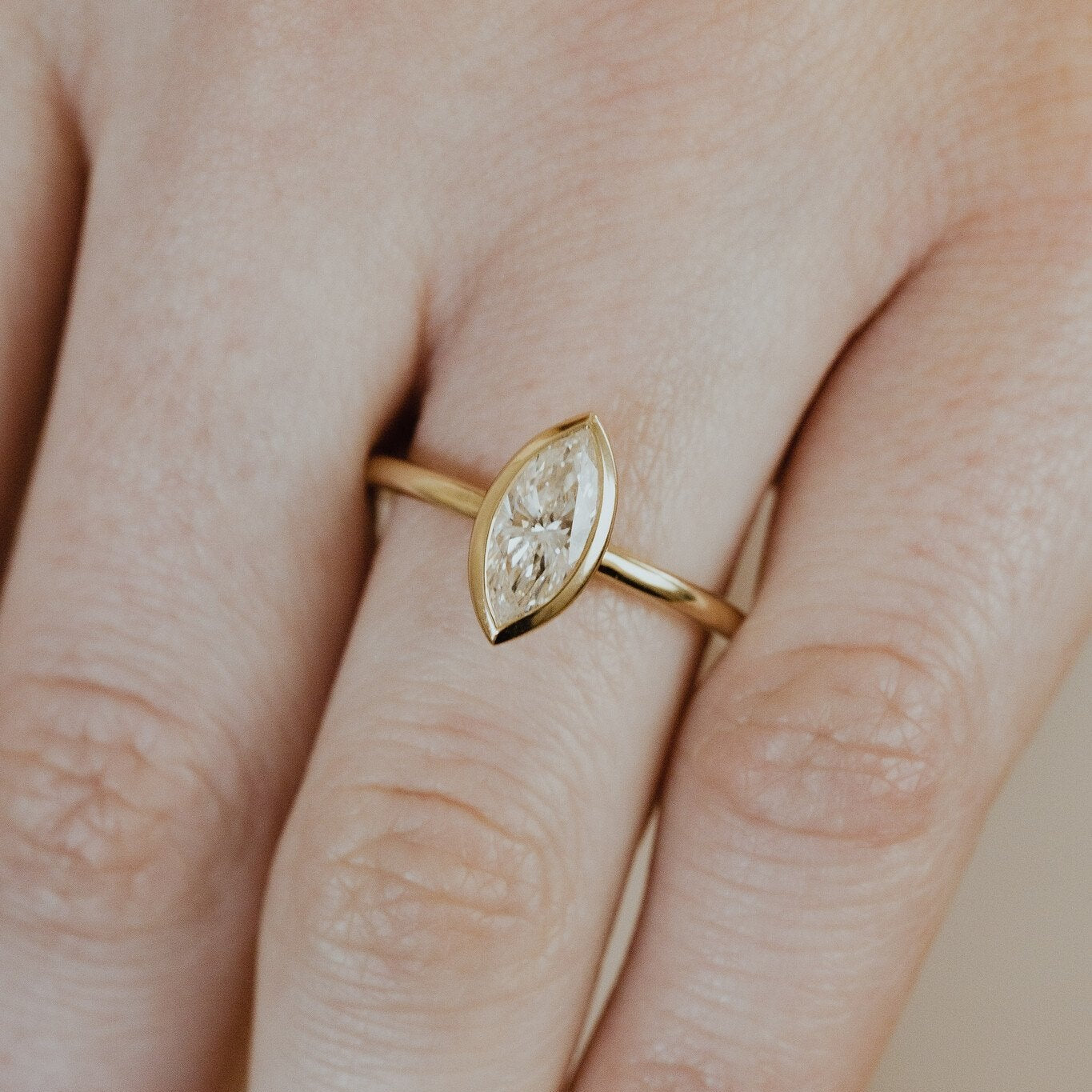 Gold bailey ring with a marquise diamond on a finger.