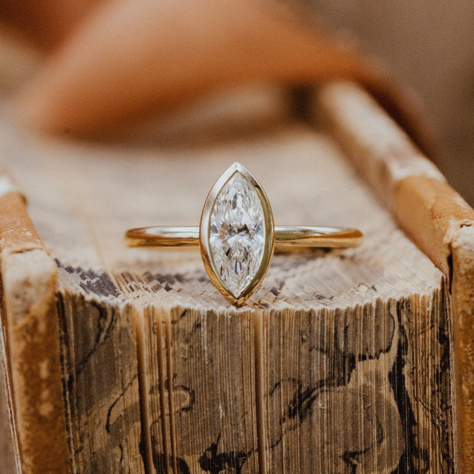 Gold Bailey ring with a marquise diamond on a wooden surface.