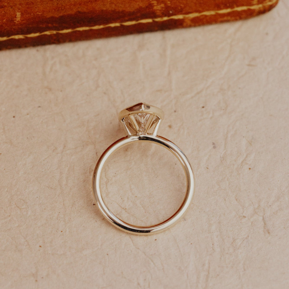 Gold Bailey ring with a marquise diamond on a beige surface.