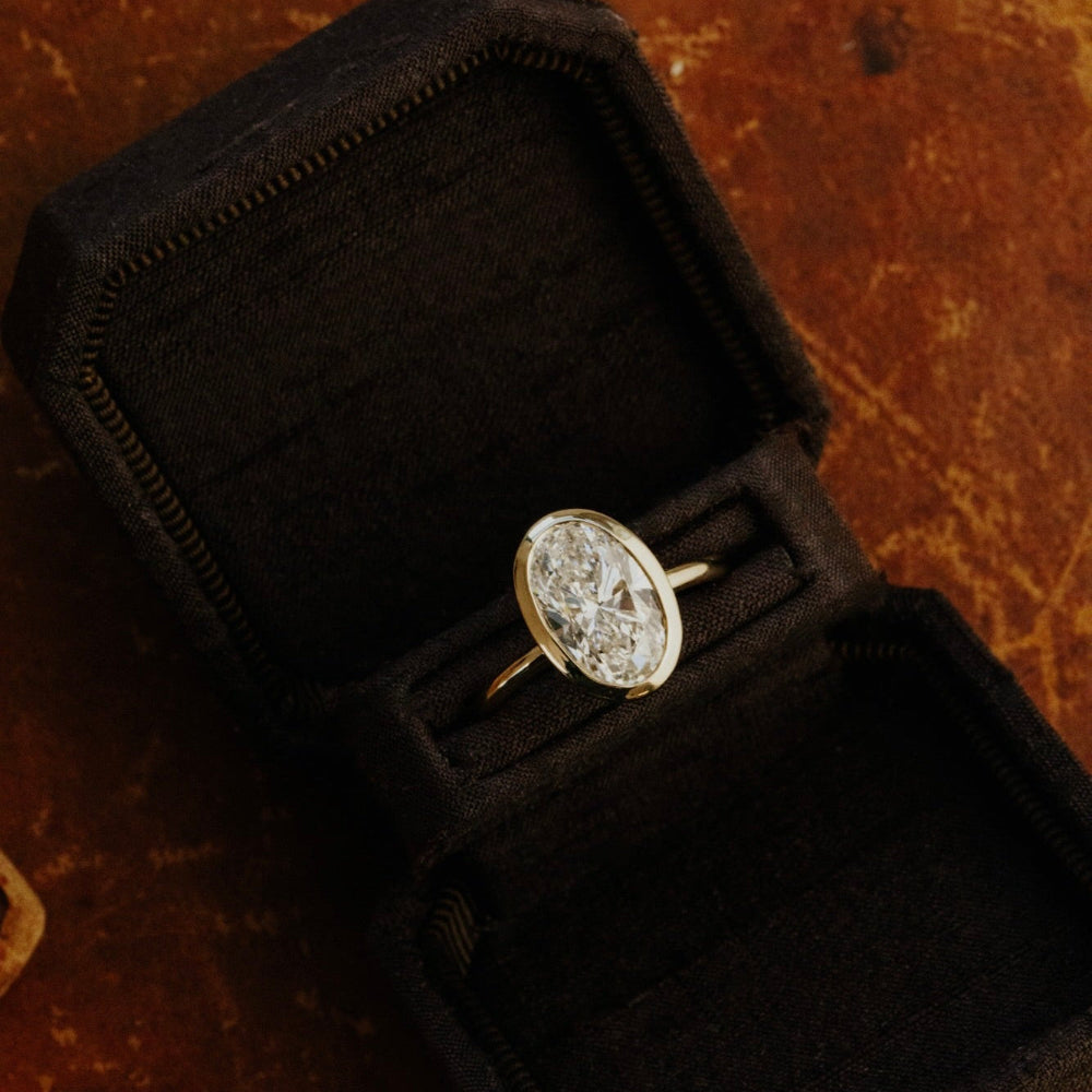 Bailey gold ring with a oval diamond in a black velvet box on a textured brown surface.