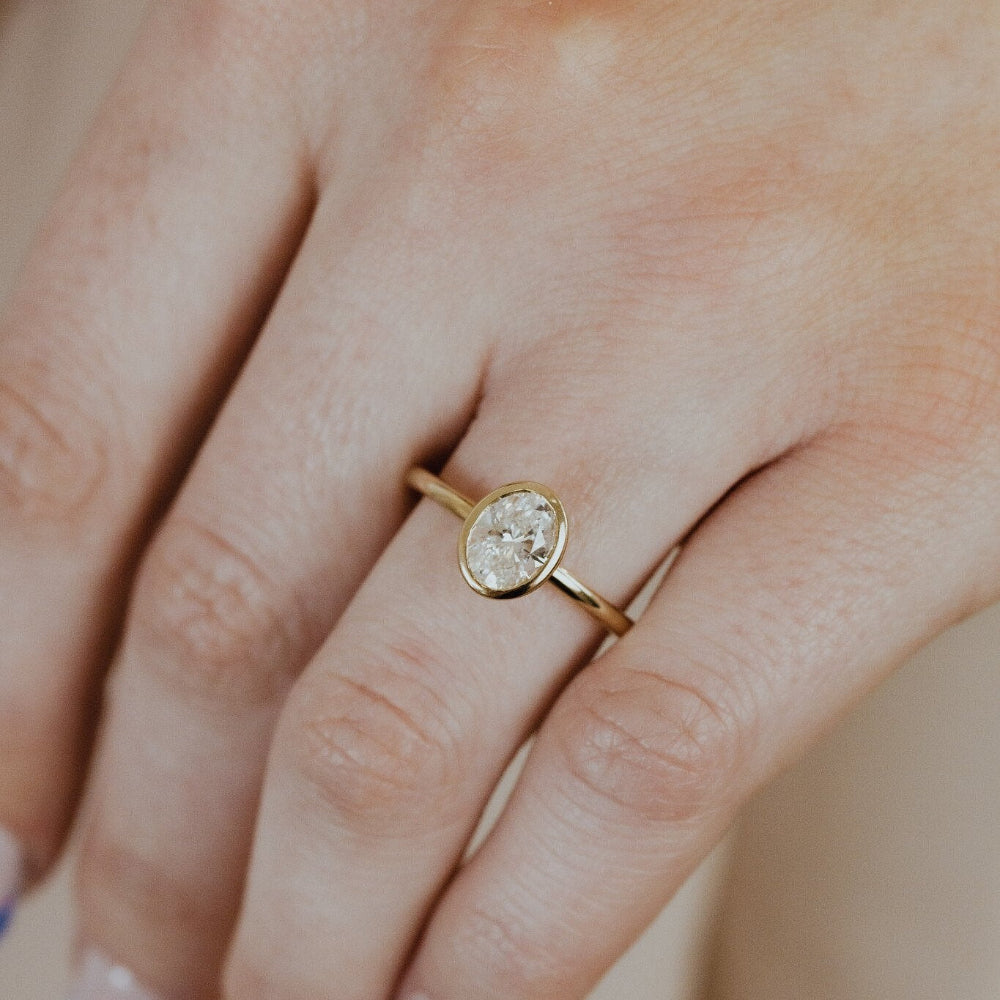 Gold Bailey engagement ring with a oval diamond on a person's finger.