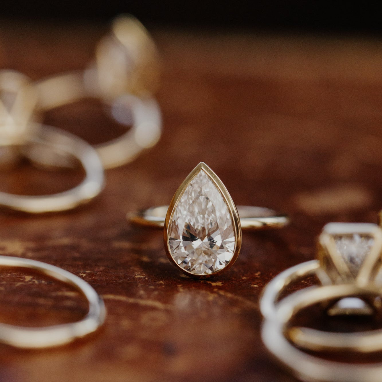 Gold Bailey ring with a pear-shaped diamond on a wooden surface.