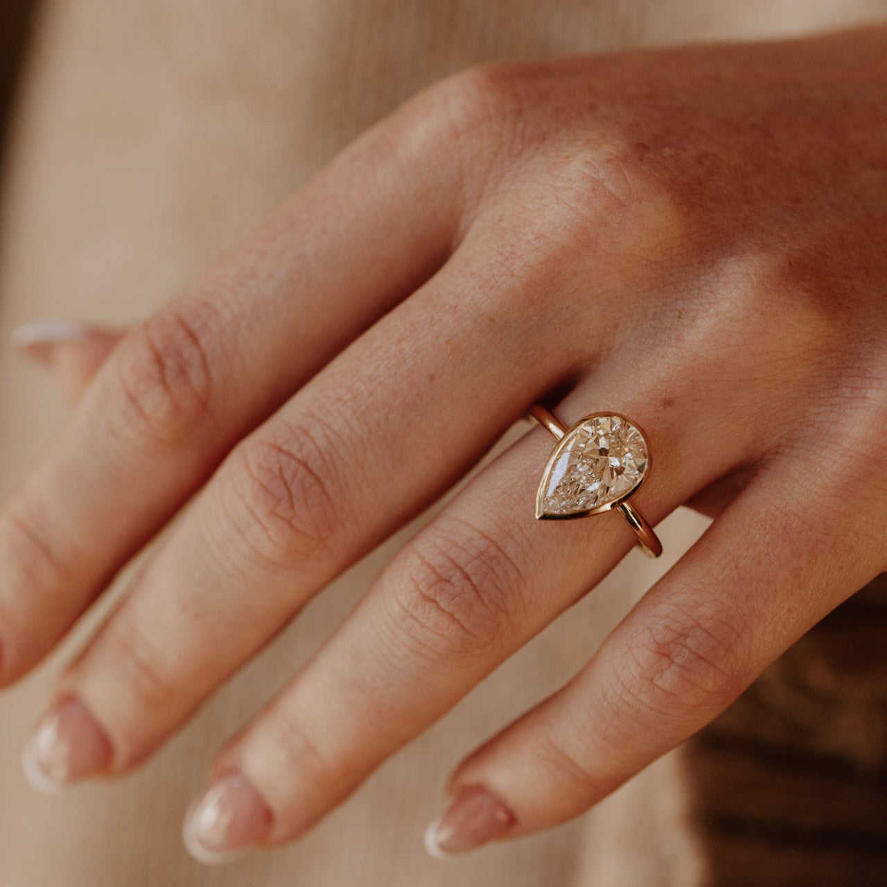 Hand wearing a yellow gold Bailey ring with a pear-shaped diamond on a neutral background.