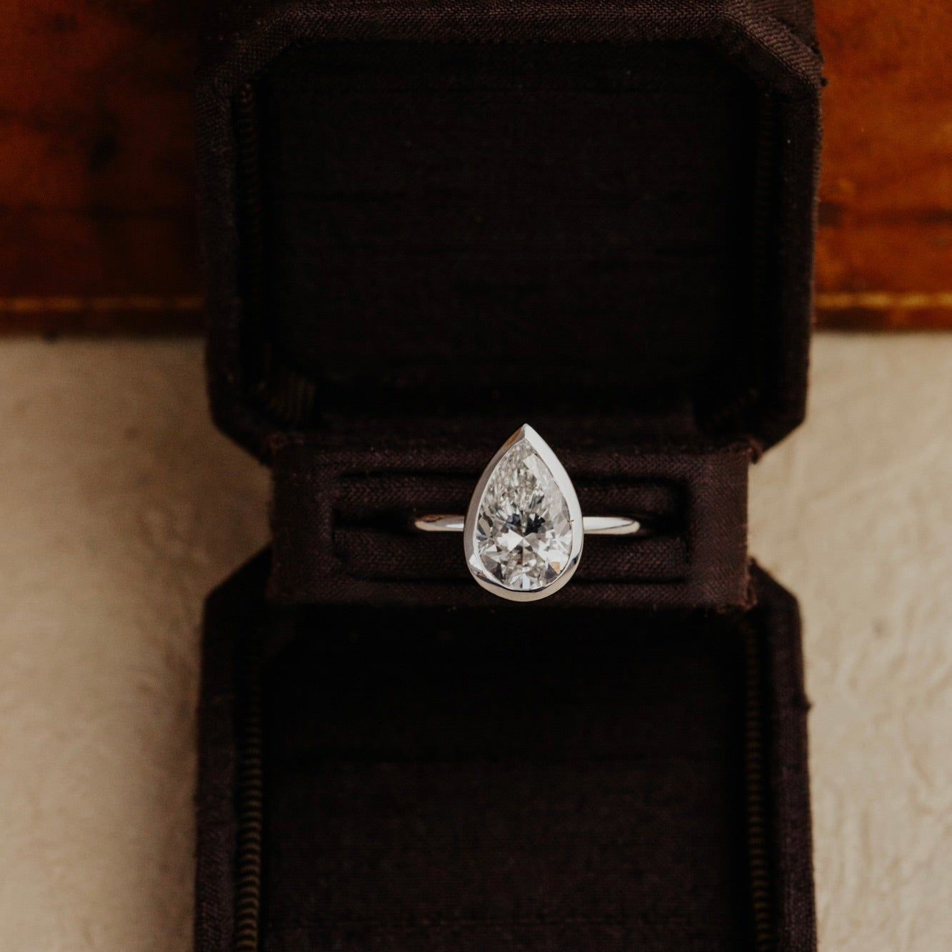 Bailey pear diamond ring in white gold in a black velvet box on a wooden surface.