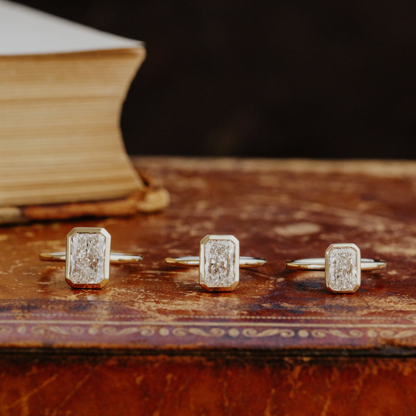 Three Bailey radiant cut diamond engagement rings in different carat weights on an old book.