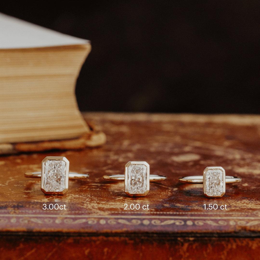 Three Bailey radiant cut diamond engagement rings in different carat weights on an old book.