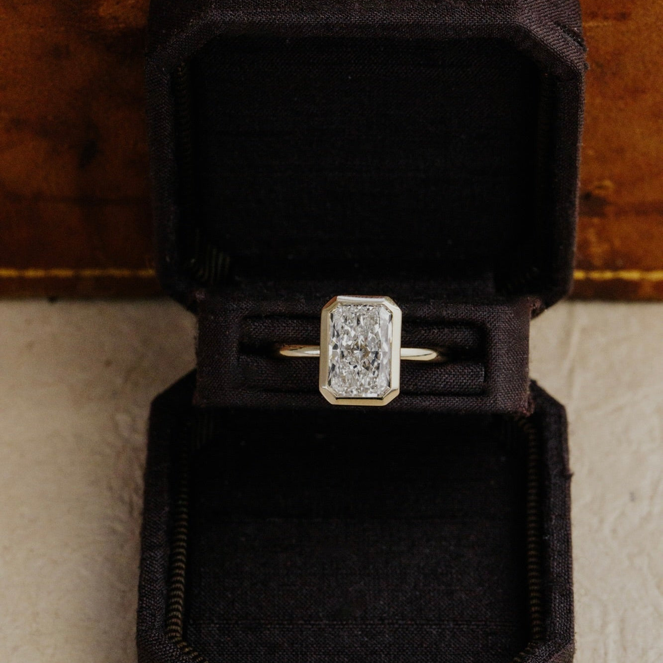 Bailey radiant cut diamond engagement ring in a black velvet box on a textured surface.