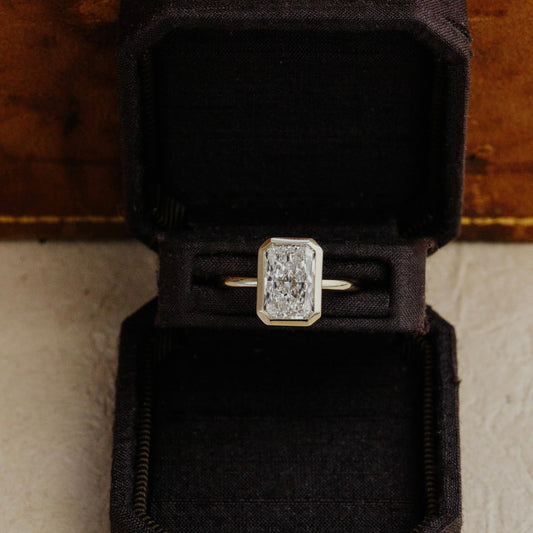 Bailey radiant cut diamond engagement ring in a black velvet box on a textured surface.
