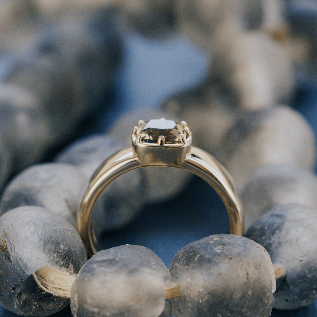A 14k gold ring with a cushion-cut green Montana Sapphire set on a textured blue background on a beaded necklace.&nbsp;