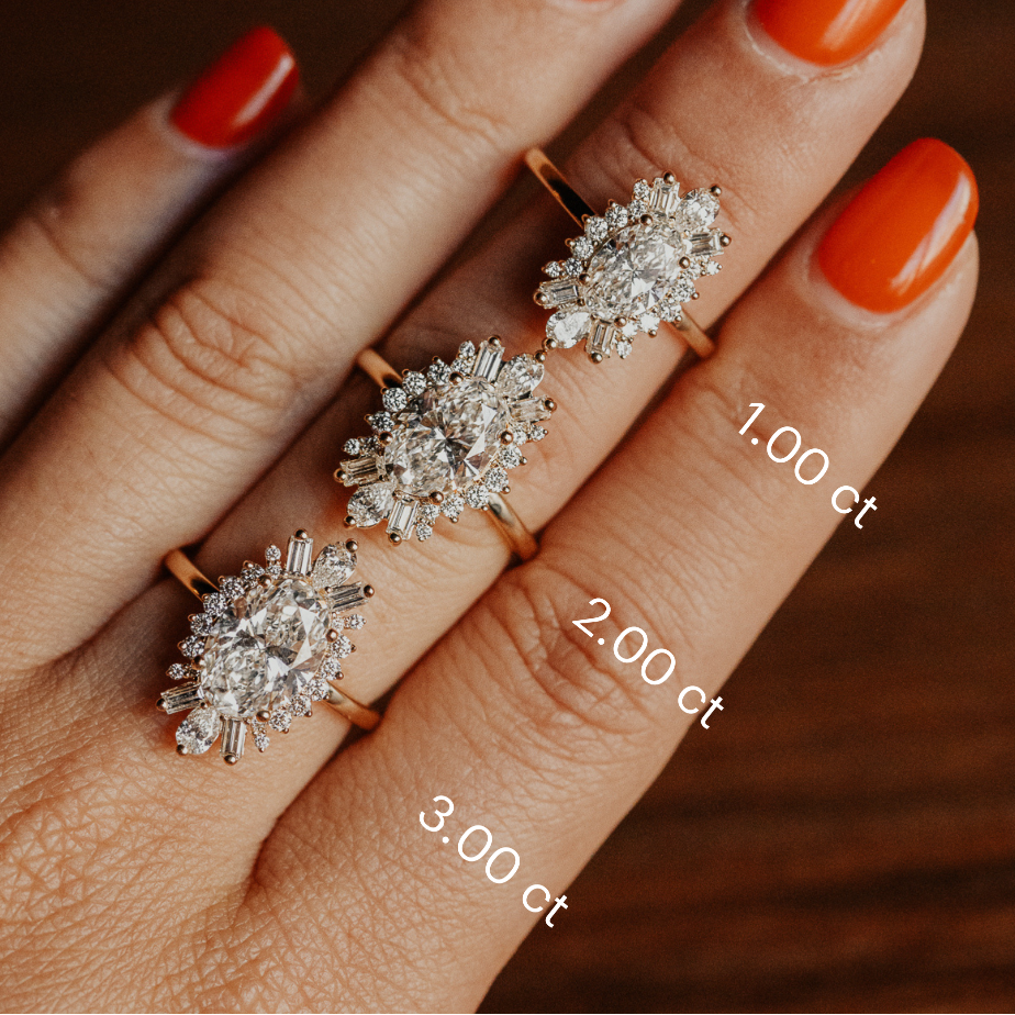 Hand wearing three Celeste halo diamond engagement rings with labeled carat weights on a wooden background.