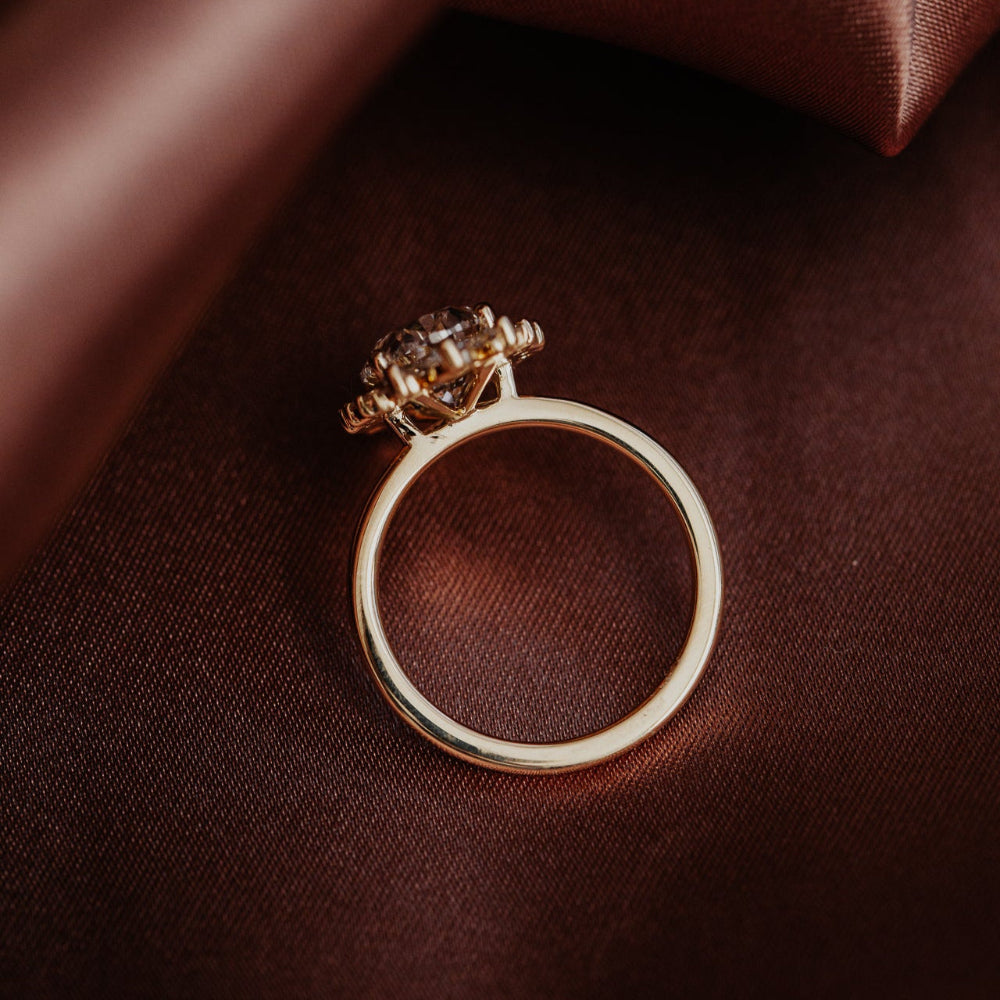 Celeste oval diamond engagement ring on a brown silk fabric.