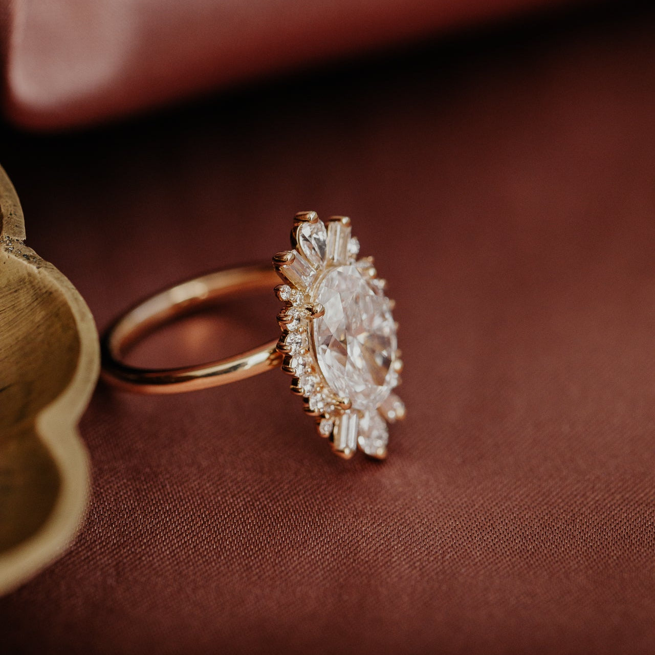 Side view of the Celeste oval diamond engagement ring on a brown silk fabric.