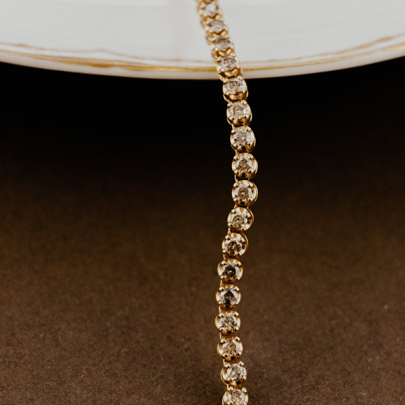 Gold champagne diamond tennis necklace on a dark surface.